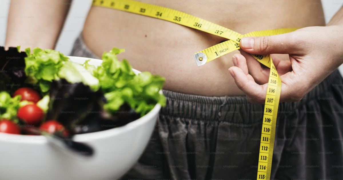 Woman measuring her waist beside a bowl of salad, illustrating weight management in PCOS